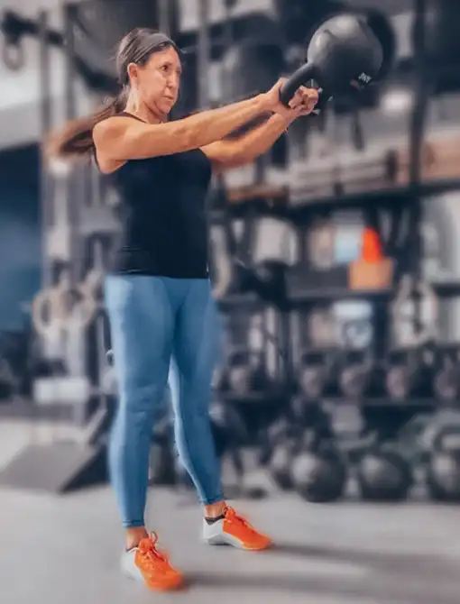 Woman performing a kettlebell swing during an online personal training workout with State of Fitness.